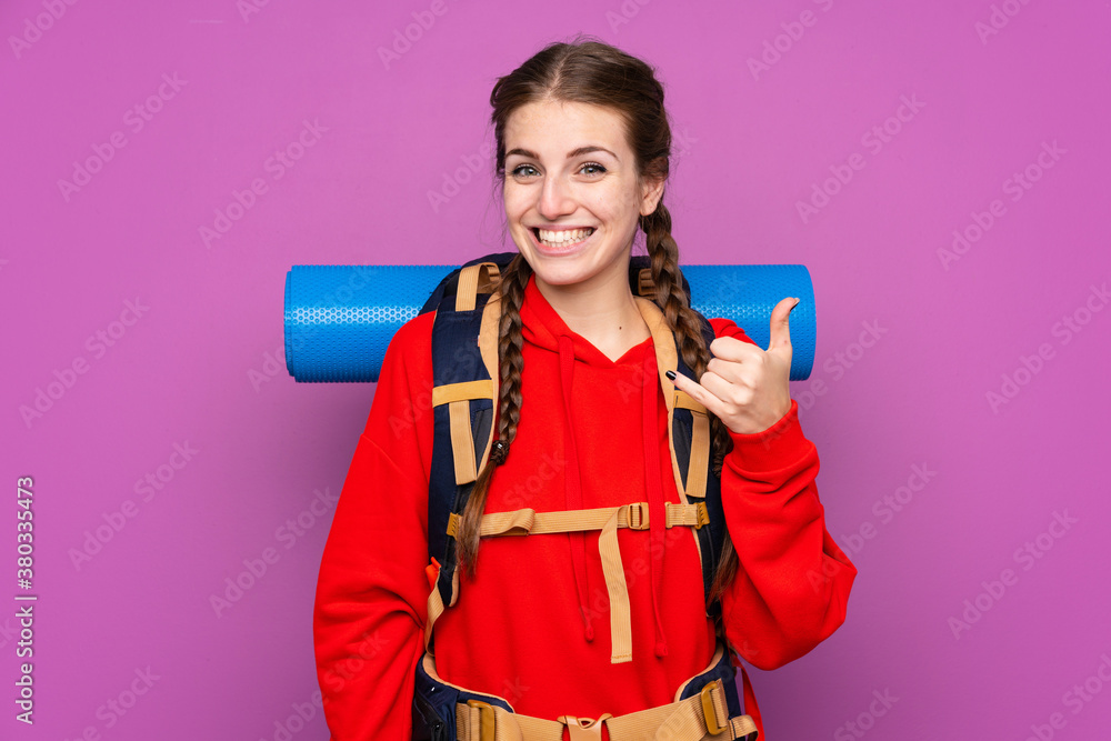 Young mountaineer girl with a big backpack over isolated purple background Young mountaineer girl with a big backpack over isolated purple background