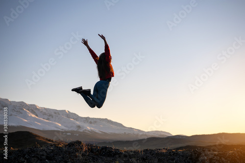 Slim girl jumps against mountains and sunset