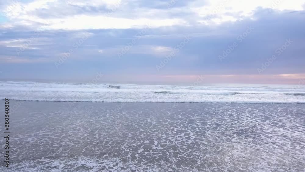 Aerial flying low over the ocean towards the horizon with sunset clouds and waves crashing on sandy beach. Aerial flying low over the ocean towards the horizon with sunset clouds and waves crashing on sandy beach.