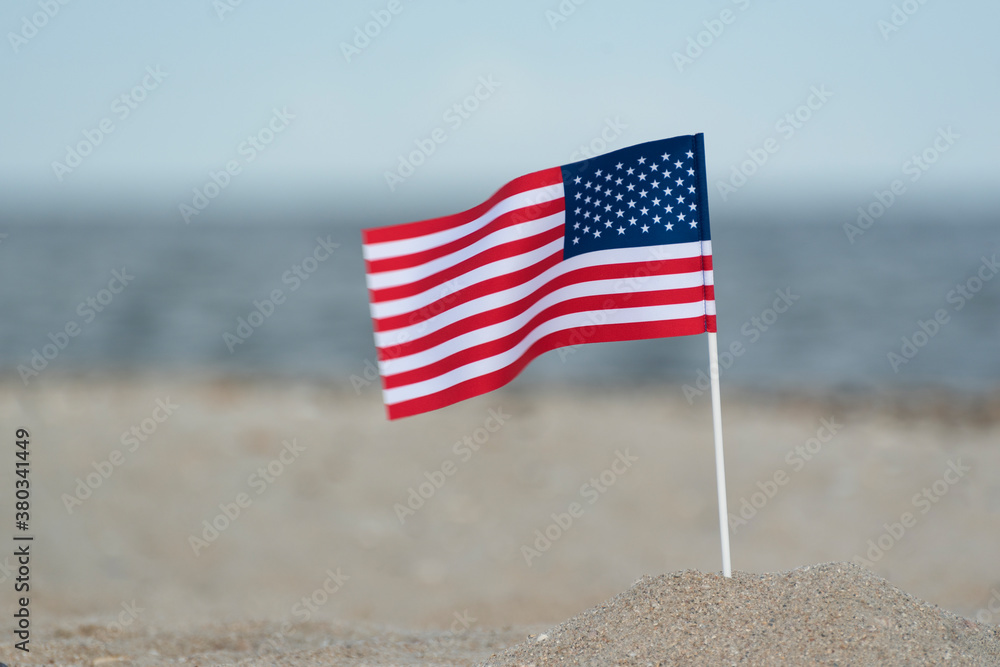 Naklejka premium Flag of United States of America on sandy shore. National flag of America, sea background.