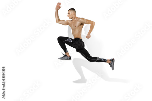 Running, jumping high. Stylish young male athlete on white studio background, portrait with shadows. Sportive fit model in motion and action. Body building, healthy lifestyle, style concept.