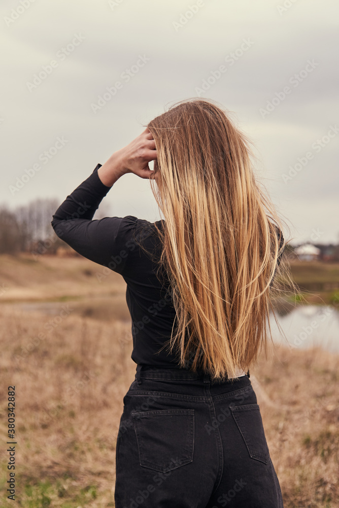 A girl with long blonde hair stands with her back to the camera against the autumn landscape. A girl with long blonde hair stands with her back to the camera against the autumn landscape.