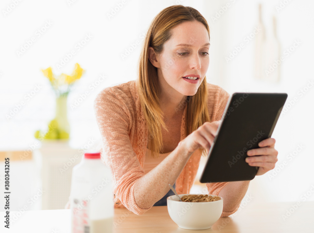 Woman eating breakfast and looking at tablet pc Woman eating breakfast and looking at tablet pc
