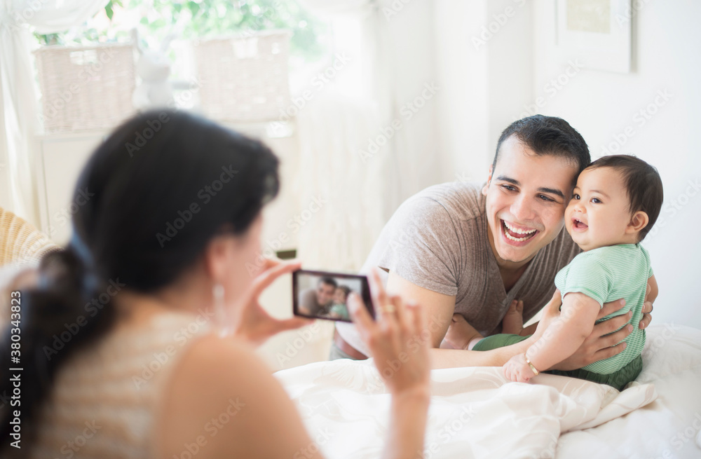 Mother photographing father with baby son (6-11 months) in bedroom Mother photographing father with baby son (6-11 months) in bedroom