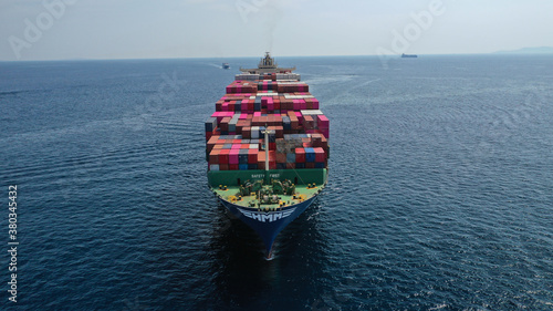 Aerial drone photo of huge container cargo Ship carrying load in truck-size colourful containers cruising deep blue open ocean sea 