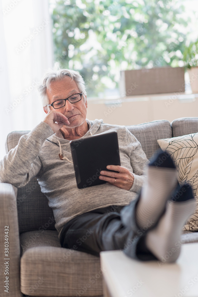 Senior man sitting on couch in living room and using tablet pc Senior man sitting on couch in living room and using tablet pc