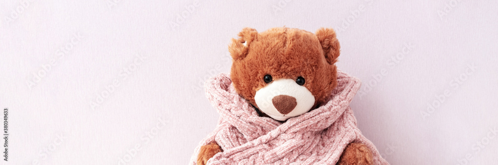 Cute classic teddy bear in knitted sweater on light pastel pink background, banner format. Cozy and warm winter