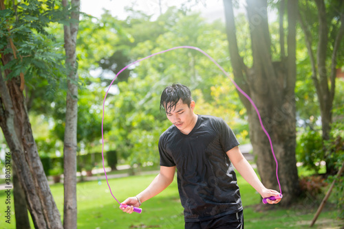 Athletic young asian man is skipping with a jump rope in the park on a summer day.