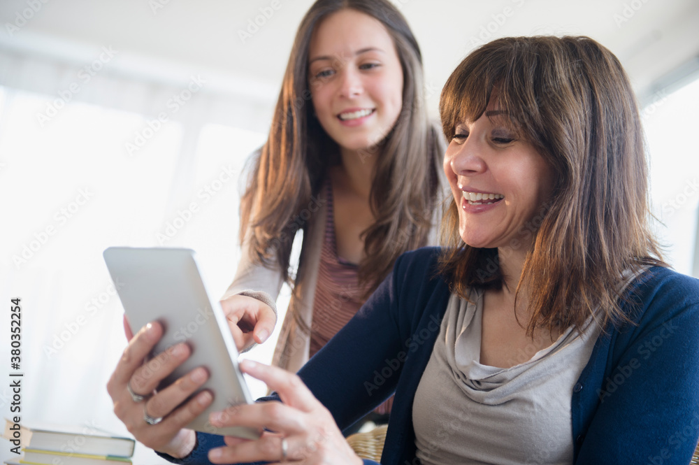 Teenage girl (14-15) using digital tablet with her mom in living room Teenage girl (14-15) using digital tablet with her mom in living room