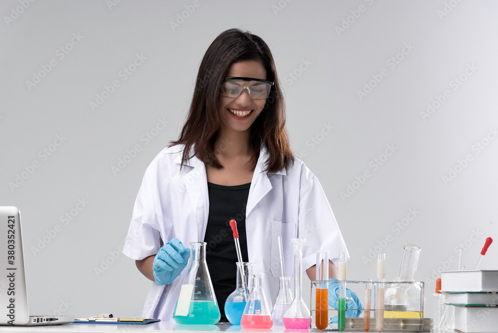 Cheerful chemist woman in lap, or graduate student in lab coat and protective wear work, check and test chemistry. Cheerful chemist woman in lap, or graduate student in lab coat and protective wear work, check and test chemistry.