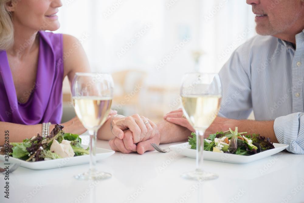 Cropped view of couple holding hands in restaurant with glasses of white wine in foreground Cropped view of couple holding hands in restaurant with glasses of white wine in foreground