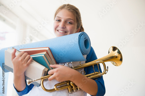 Portrait of teenage girl (12-13) holding rolled-up exercise mat, books, and trumpet