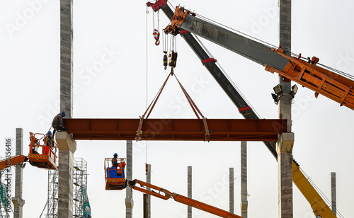 Construction workers installation steel structure girder runway beam lifting by mobile crane and placing on corbel of column concrete at the construction site project