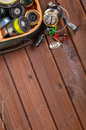 Different fishing tacles with lures and reels on wooden brown background with place for text.