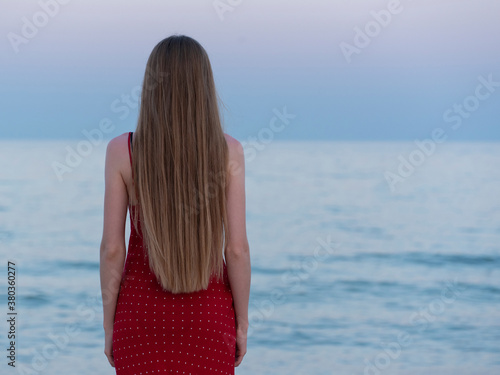 The girl stands with her back to the frame and looks into the distance of the sea