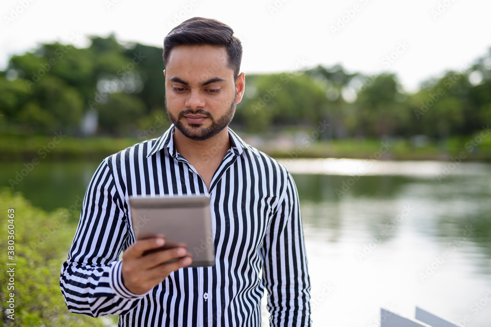 Young bearded Indian businessman relaxing at the park in the cit Young bearded Indian businessman relaxing at the park in the cit