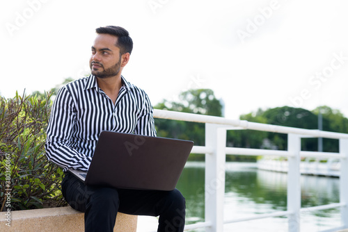 Young bearded Indian businessman relaxing at the park in the cit
