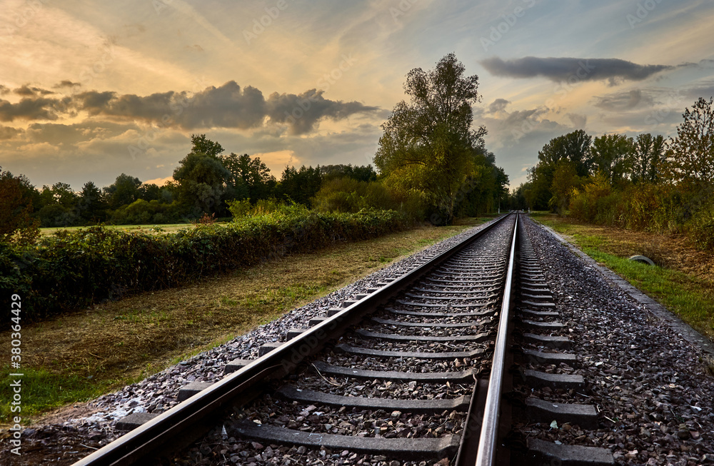 Fototapeta premium Train tracks through rural landscape against cloudy sky at sunset