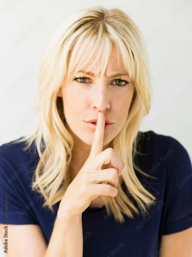 Studio portrait of blonde woman with finger on lips Studio portrait of blonde woman with finger on lips