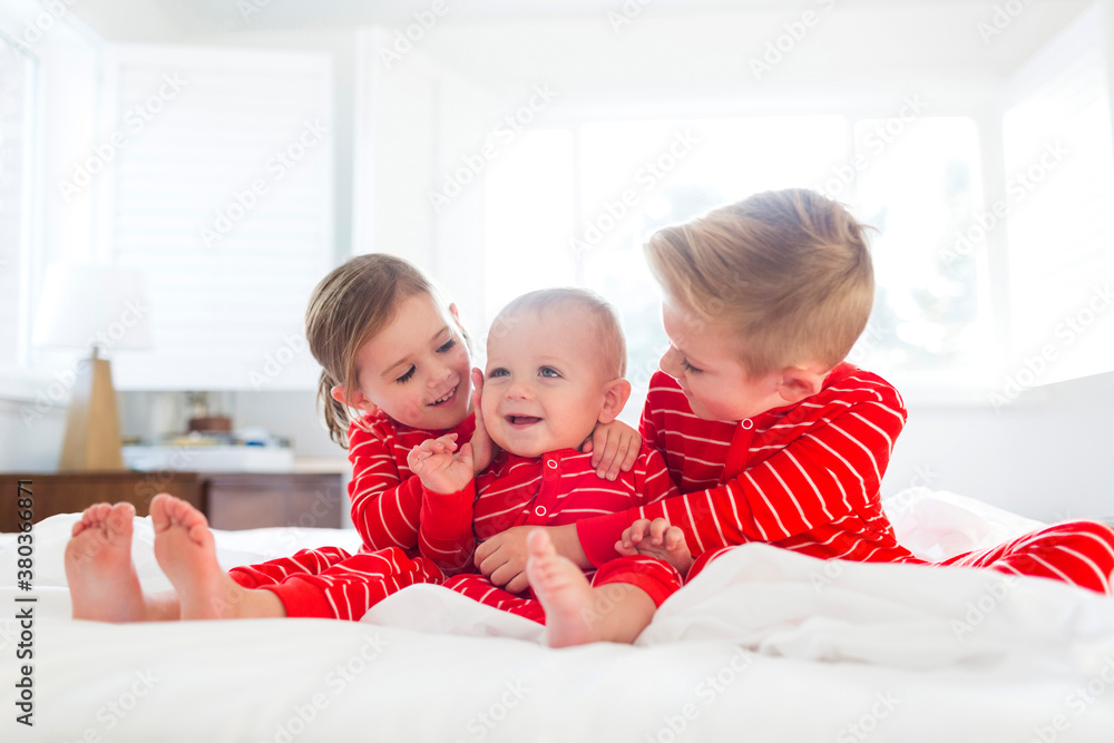 Boy (6-7) and girl (4-5) embracing brother (2-3) on bed Boy (6-7) and girl (4-5) embracing brother (2-3) on bed