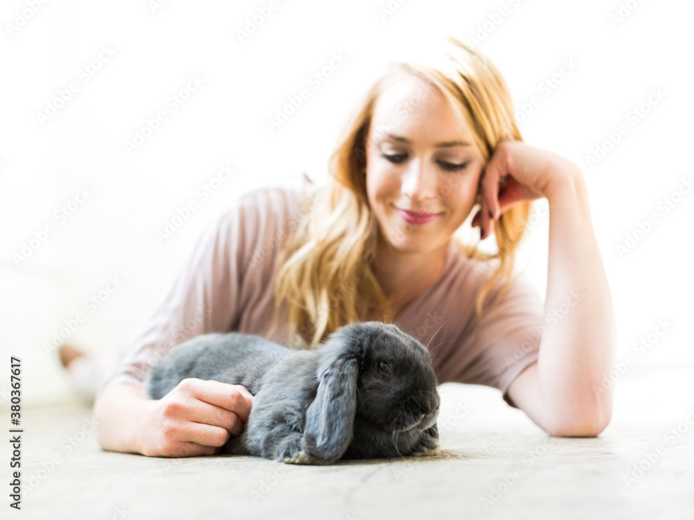 Young woman lying on floor and stroking rabbit Young woman lying on floor and stroking rabbit
