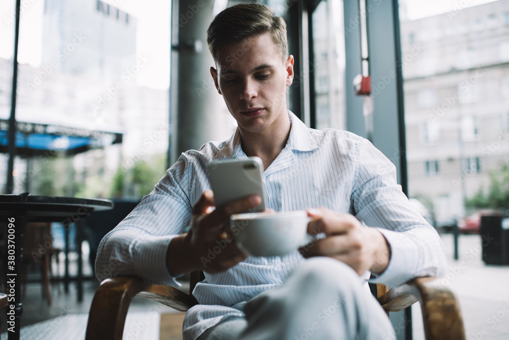 Concentrated man with cup of coffee using smartphone Concentrated man with cup of coffee using smartphone
