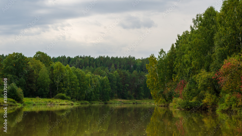 Autumn view from the surface of the lake on the shore overgrown with deciduous forests. Trees reflection on calm water. Autumn landscape. forest river in the beginning of Autumn. Autumn view from the surface of the lake on the shore overgrown with deciduous forests. Trees reflection on calm water. Autumn landscape. forest river in the beginning of Autumn.