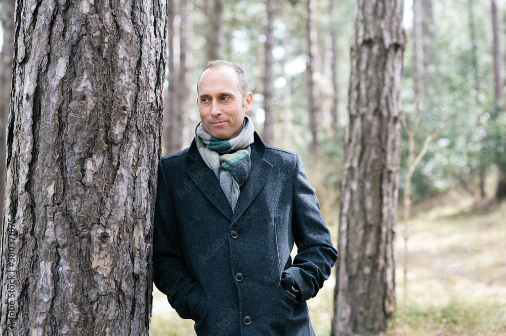 Man smiling and casually leaning against a pine tree in a wood Man smiling and casually leaning against a pine tree in a wood