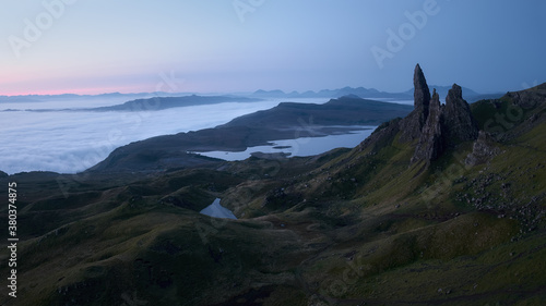 Atmospheric mysterious top view of the high sharp cliffs towering over the lakes and the sea covered with low clouds before dawn. The Old Man of Storr, The Isle of Skye, Scotland, UK.
