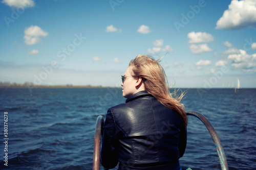 Blonde adolescent girl sitting at a pier overlooking a lake photo