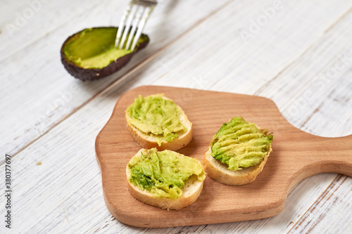 Baguette, bruschetta, canapes with avocado on a light wooden background.