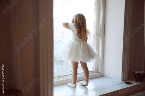 a little girl in a smart, fluffy white dress near the window and waits for Santa Claus or the tooth fairy. children's fairy tales and dreams. new year holiday.