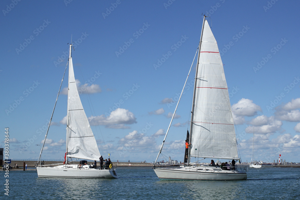 two beautiful white sailboats are sailing in the in the sea at the dutch coast in Breskens during an ocean race in summer and a blue sky