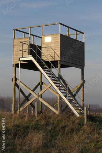 a big wooden bird observatory tower in a nature reserve in zeeland the netherlands in winter, to watch over big green fields with roe deers