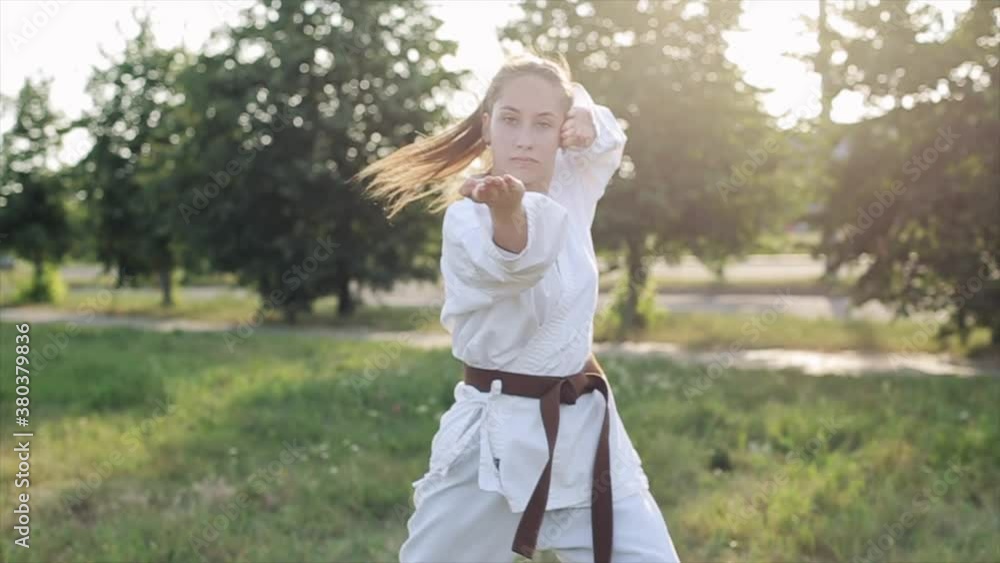 A young woman in a white kimono demonstrates karate techniques in martial arts training against the backdrop of nature. Close-up A young woman in a white kimono demonstrates karate techniques in martial arts training against the backdrop of nature. Close-up