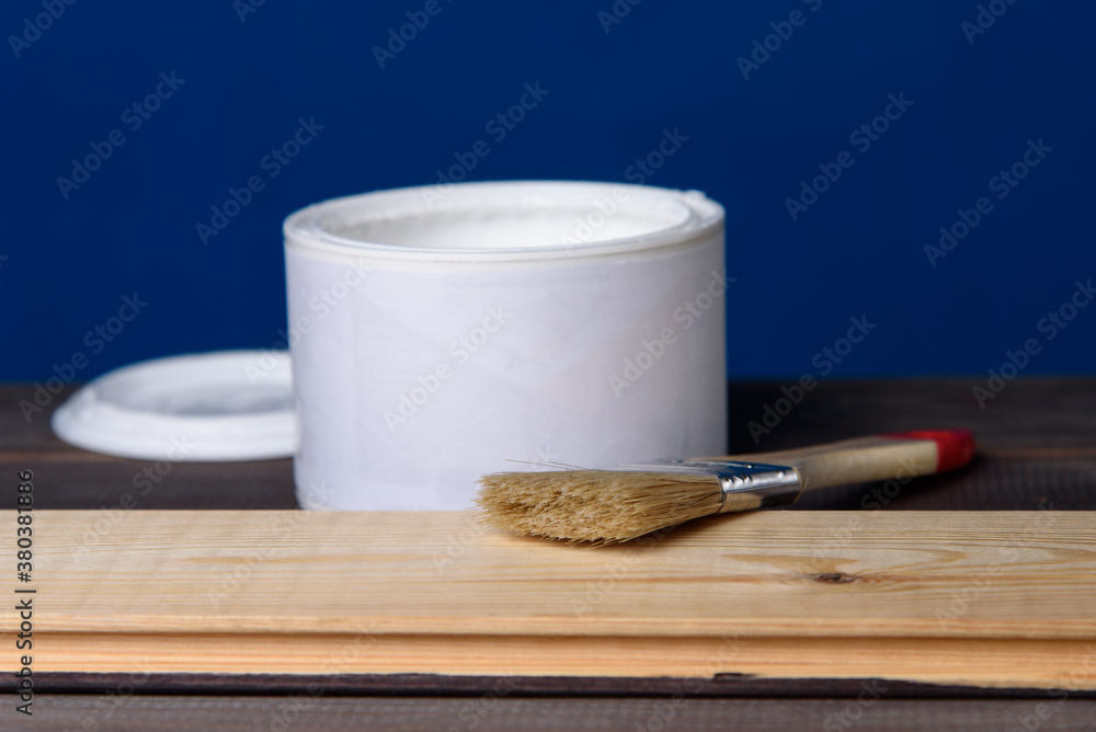 A can of white paint and a paintbrush on a wooden table