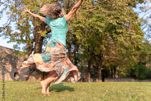 Beautiful barefoot girl in a long colorful skirt is dancing in natural background