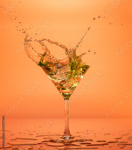 Fotografía Vermouth cocktail splashing out of a martini glass isolated on orange backdrop