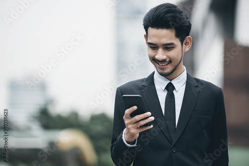 Young executive businessman using a mobile phone in the business district with skyscrapers buildings background	
