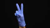 Female hand in a latex medical glove makes an peace gesture isolated on black background.