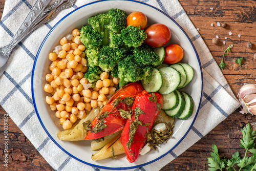Cooked chickpeas with vegetables. Boiled chickpeas with broccoli, baked peppers, tomatoes and cucumbers in a plate on a wooden background top view. Vegetarian and vegan food.