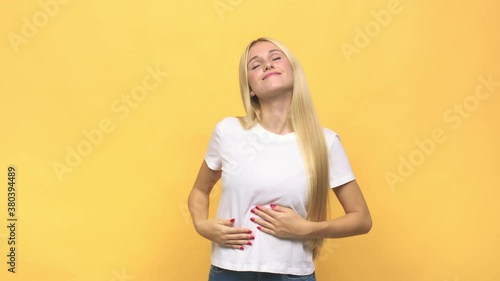 Young caucasian blonde woman touches tummy, smiles gently, eating and satisfaction concept
