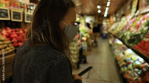 Pretty young woman holding trolley for collecting fruits and vegetables looking around for fresh fruits and vegetables in departmental store