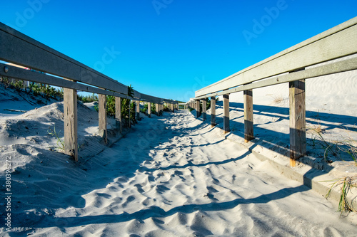 A Sandy Beach Path With a Wooden Fence on Each Side Casting Various Shadows © HRTNT Media