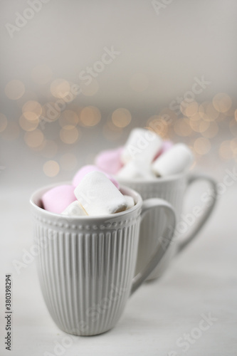 Fototapeta Naklejka Na Ścianę i Meble -  Hot winter drink with cocoa and marshmallows in mugs on wooden white background with Christmas garland. Top view.
