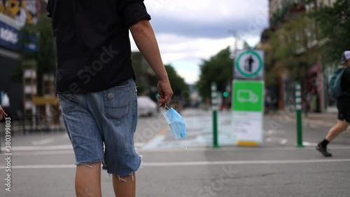 Selective focus of young male hands holding covid-19 surgical face protective mask while taking a walk on streets of downtown photo