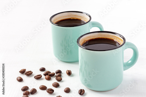 Two blue cups of fresh aromatic coffee with grains on white wooden background. Copy space