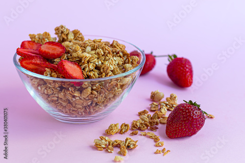 Homemade granola with strawberry slices on a pink background. Vegetarian dish. Healthy breakfast.