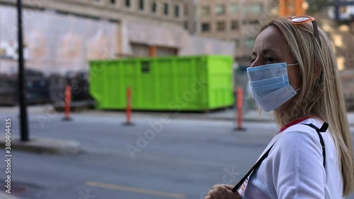 Female wearing covid-19 protective face mask to fight against coronavirus with a purse walking on street with sunglasses on head