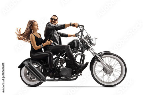 Biker in a leather jacket riding a young woman on a chopper motorbike and looking at her
